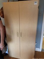 Closed front view of light-colored press board cupboard cabinet with two vertical doors and recessed handles.