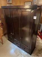 Front view of solid wood cabinet showing three paneled doors and three drawers beneath with round wooden knobs.