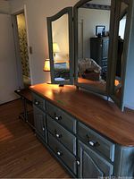 Overall view of green-stained dresser with natural wood top and attached tri-fold mirror.