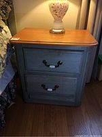 Front view of end table showing natural wood top and bluish-green stained drawer base with lamp on top