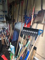View showing various garden tools including rakes, shovels, and a black snow shovel hanging on the wall.