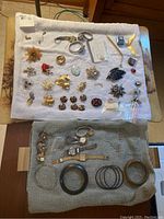 Wide view of assorted costume jewelry items including brooches, earrings, and bracelets on towel, showing variety and some damage.