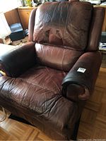 Front full view of large brown leather recliner with visible creases and wear on seat and arms.