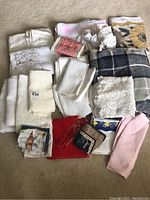 View of assorted folded linens including embroidered doilies, patterned cloths, and plain colored napkins and fabrics arranged together.
