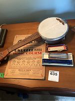 Photo of small banjo, two harmonicas in cases, and vintage ukulele/banjo course booklet arranged on table