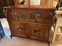 Front view of cabinet showing decorative metal scrollwork and drop handles