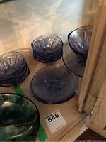 Stack of purple glass plates, dessert bowls, serving bowl and platter inside a cabinet.