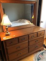 Photo of solid wood dresser with 8 drawers and attached large framed mirror, lamp on top and bedroom reflected in mirror.