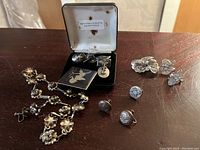 Photo showing sterling jewelry laid on table including floral necklace, butterfly brooch earring set in case, and various other brooches and earrings