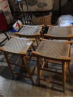 Four wooden framed stools with woven plastic seats arranged together, showing overall look and height.