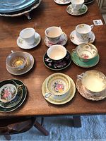 Overview of all nine teacups and matching saucers arranged on a wooden table showing various patterns and colors.