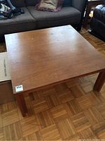 View of the square teak coffee table from above showing the wood surface and wear marks.