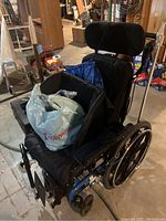 Blue-framed STP Power Plus manual wheelchair with cushioned black seat, adjustable armrests, headrest, and accessories placed on the seat.