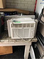 Full front view of the Haier window air conditioner on a wooden bench with visible power cord and control panel.