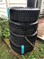 Stack of four black Goodyear winter tires with blue labels, showing tread pattern and general condition.