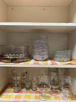 Shelves holding clear glass bowls, some with textured surfaces, stacked small glasses, and various drinking glasses including etched tumblers and snifters.