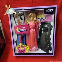Collector's edition Barbie doll in box showing doll wearing pink satin gown and feathered boa, alternate black glittery dress, and booklet inside purple packaging.