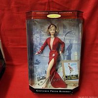 Full view of Barbie doll in original box showing red dress, doll styling, and included booklet.