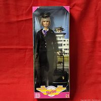 Full front view of Barbie doll in original box with pilot uniform, hat, scarf, and rolling carry-on bag.