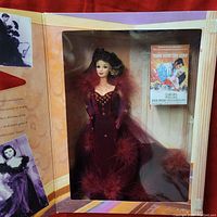 Barbie doll displayed in original box with gold star-shaped window, showing doll in red velvet gown with feather trim.