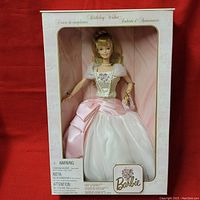Barbie doll in original box wearing white and pink dress with floral embroidery and pearl necklace.