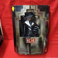 Front view of Cruella de Vil Barbie doll in original packaging showing doll in black pinstripe outfit with white collar and black hat.