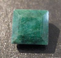 Front view of square cut emerald gemstone showing deep green color and natural inclusions.