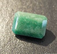 Close-up photo of a rectangular emerald-cut green gemstone showing natural inclusions and reflective facets.