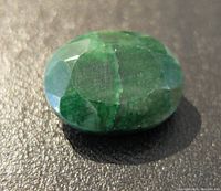 Close-up front angled photo of oval faceted emerald gemstone showing facets and natural inclusions in green color.