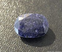 Close-up of the oval faceted blue sapphire gemstone highlighting surface texture and inclusions under light.