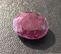 Close-up photo of the oval cut ruby gemstone showing red and pink colors with surface inclusions under direct lighting.