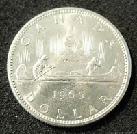 Obverse side of the 1965 Canadian silver dollar coin showing the Voyageur design with two men paddling a canoe and the year 1965.