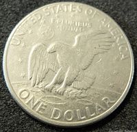 Reverse side of the 1972 US one dollar coin showing an eagle landing on the moon, inscriptions include UNITED STATES OF AMERICA, E PLURIBUS UNUM, and ONE DOLLAR.