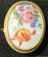 Front view of oval vintage porcelain brooch with pastel floral design and gold-tone twisted rope border.