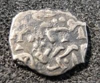 Close-up of one side of the small ancient coin showing worn symbols and irregular edges
