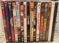 Side view of 16 DVD cases standing upright showing titles and cover spines