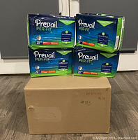 Four sealed packs of Prevail Per-Fit adult unisex daily underwear/diapers in medium size displayed on top of a sealed cardboard box likely containing more diapers.