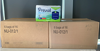 Two large cardboard boxes labeled NU-012/1 each containing 6 bags of Prevail Nu-Fit Daily Briefs, size Medium, 16 count per bag, stacked side by side with one individual bag placed on top for display.