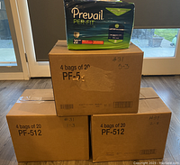 Three cardboard boxes stacked; two on bottom, one on top. One retail package of Prevail Per-Fit Adult Unisex Daily Underwear/Diapers in green packaging placed on top box for display.