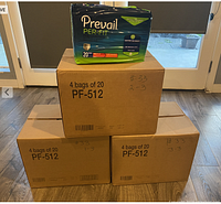 Three sealed boxes each labeled with product code PF-512 containing multiple bags of Prevail Per-Fit Adult Unisex Daily Underwear/Diapers, Medium size (34-46 inch waist). One bag is displayed on top for visual reference.