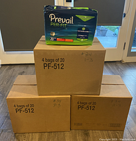 Photo showing three closed cardboard boxes labeled '4 bags of 20 PF-512' with handwritten #34, each containing 4 bags of Prevail Per-Fit Adult Unisex Daily Underwear/Diapers Medium size. One bag displayed on top of a box for product view.
