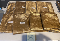 Seven pieces of gold crinkled crushed table covers displayed on a surface; six pieces are in original clear packaging and one piece is unpackaged and folded.