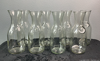 Front view of 8 clear vintage glass milk bottle carafes with an embossed circle pattern on each, placed on dark fabric