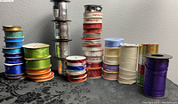 Overall view showing various colored ribbons including metallic and sheer types on spools, arranged on a dark floral surface.