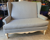 Front view of the blue and white plaid upholstered loveseat showing wingback design, padded arms, cushion, and legs.