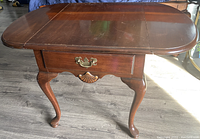 Front view of the cherry drop leaf table showing single drawer, cabriole legs, and wood finish with some wear.