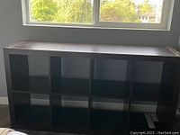 Frontal view of IKEA black-brown shelving unit showing 10 open cubes, placed near window with natural light.