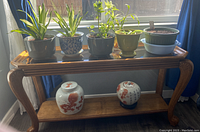 Table shown with several potted plants on top and decorative ceramic jars on lower shelf, plants and jars not included in sale.
