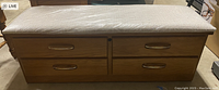 Front view of the cedar chest showing the wood finish, four drawers with handles, and cushioned top with protective covering.