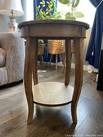 Front view of a round wood side table showing the curved legs and lower shelf